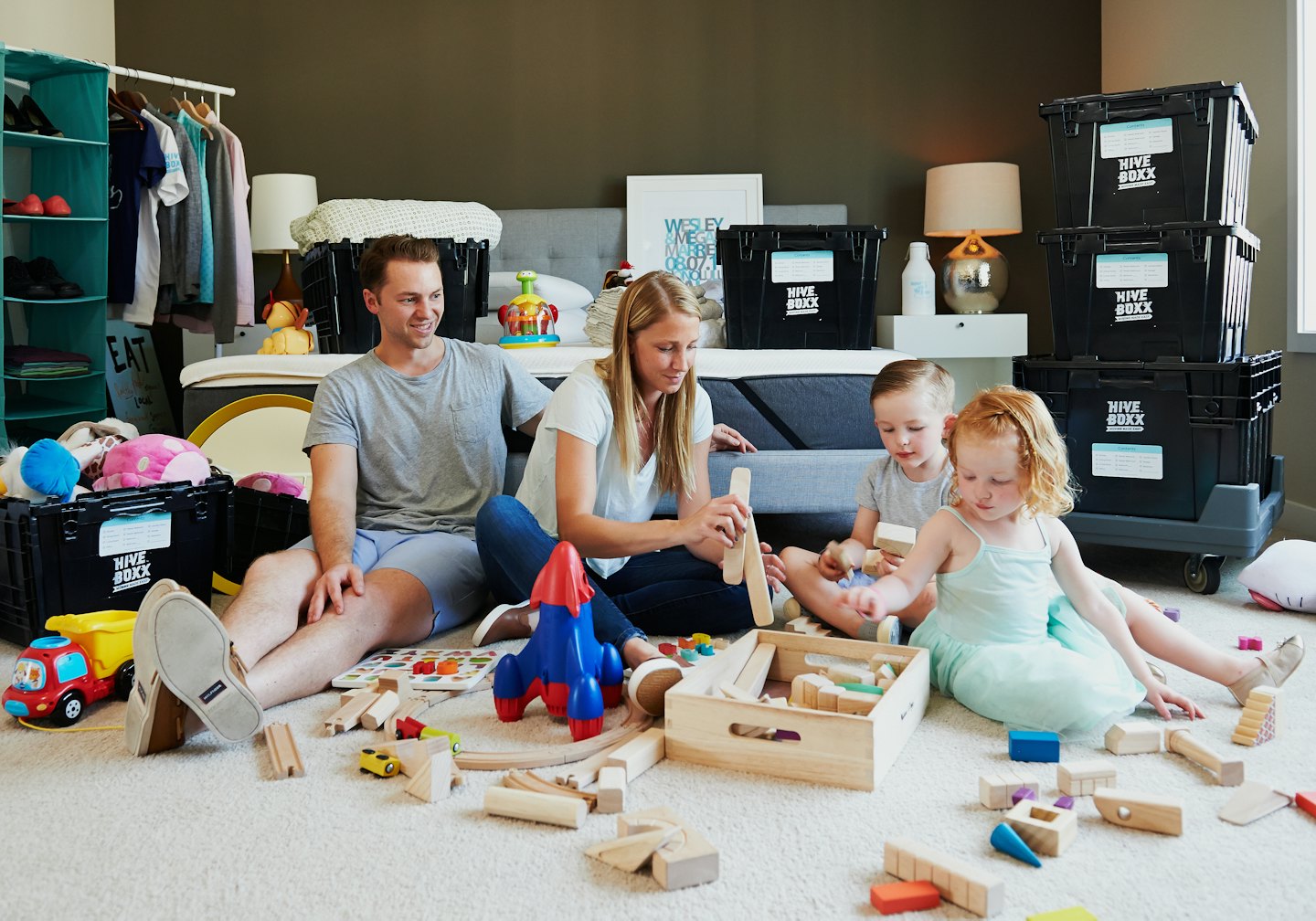 Family sitting on a carpet unpacking boxes in a new bedroom.